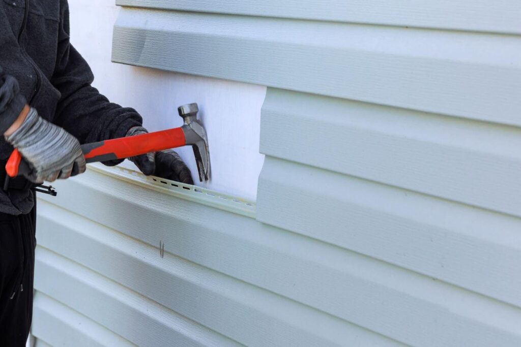 A person is using a hammer to fix siding on a wall.