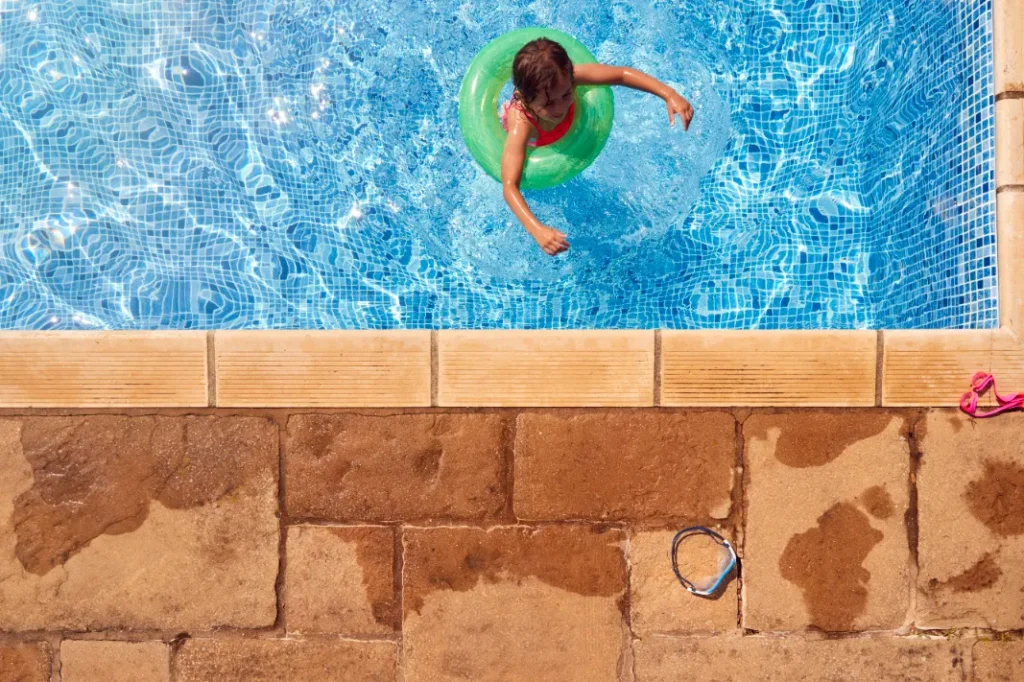 A girl splashes water out of a pool onto the surrounding paver stones.