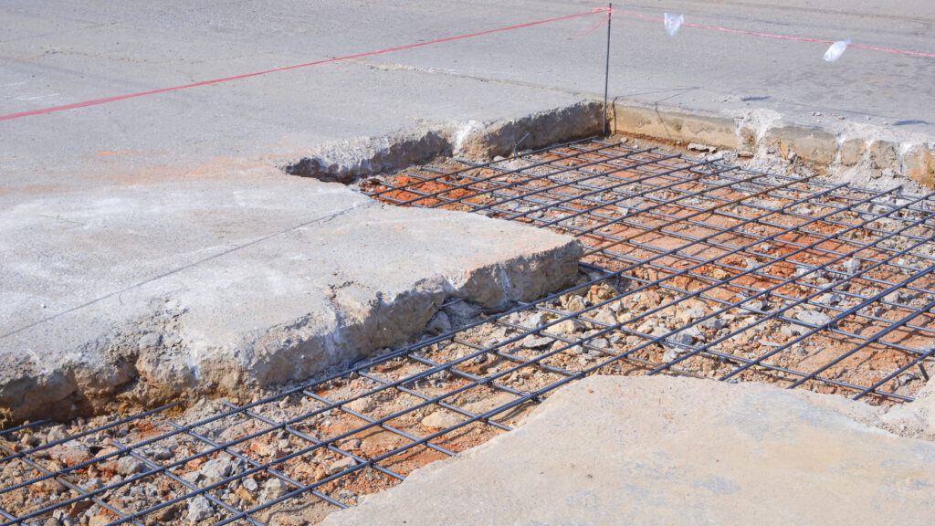 A damaged concrete walkway for repair with reinforced steel bars and concrete leveling.