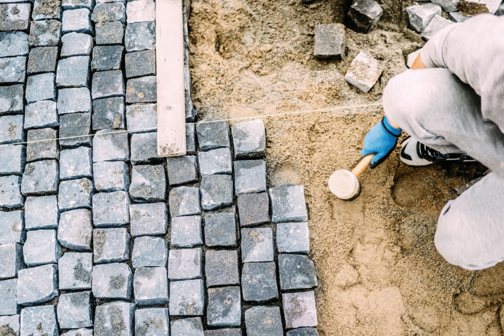 Cropped shot of a paving company worker installing stone pavers on a sand base for a commercial walkway.