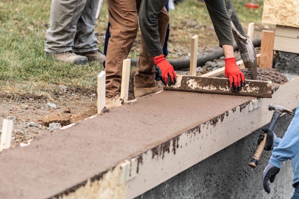 A worker runs a level over freshly poured concrete to level it off in its wood frame.