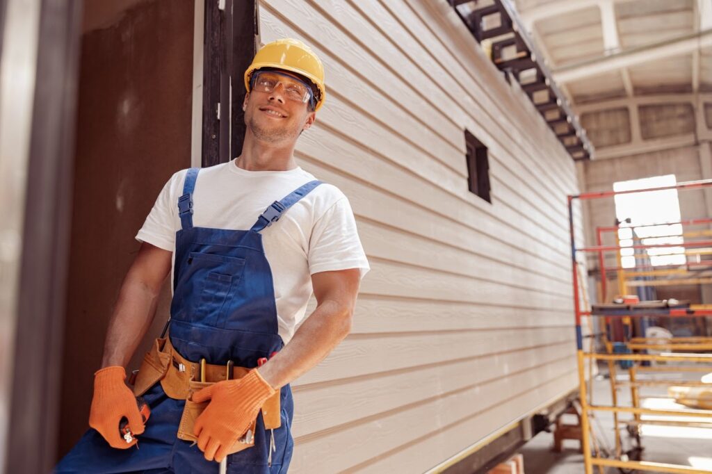 A worker stands next to a freshly-completed siding installation.
