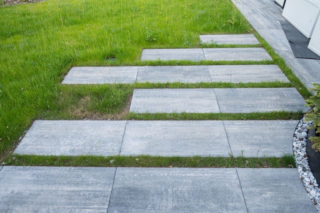 Closeup of a disconnected concrete sidewalk through a patch of grass.