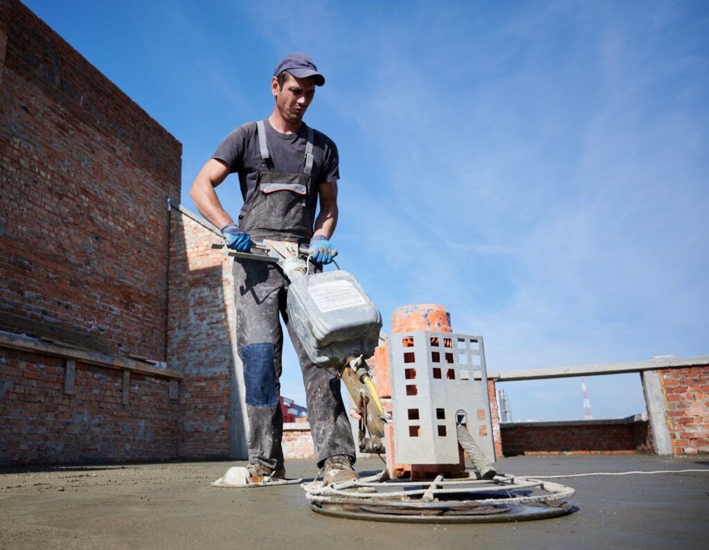 A worker uses a machine to level and smooth freshly poured concrete.