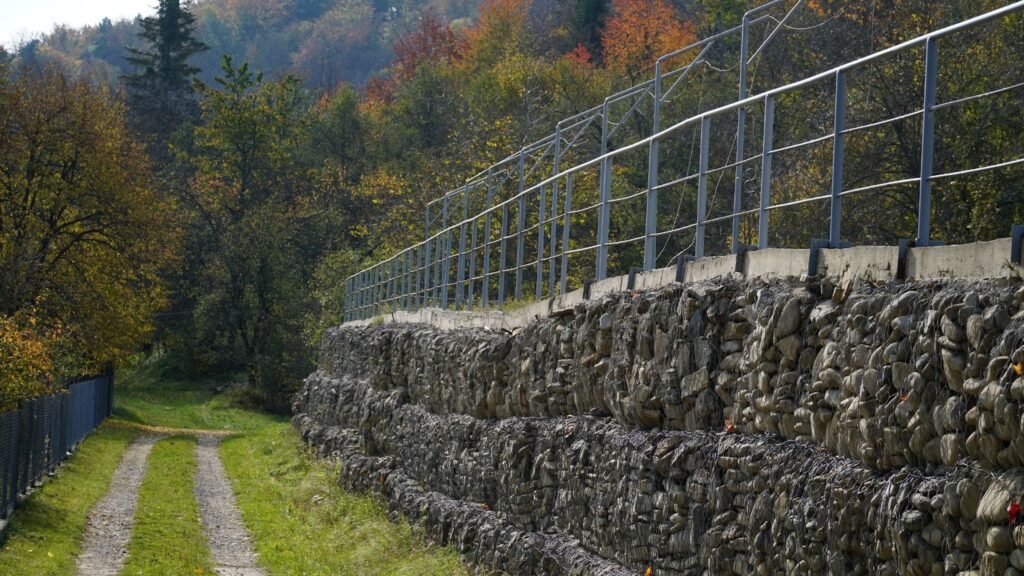 Metal grate holding granite stones in place as structural support for slope-stabilizing retaining walls.
