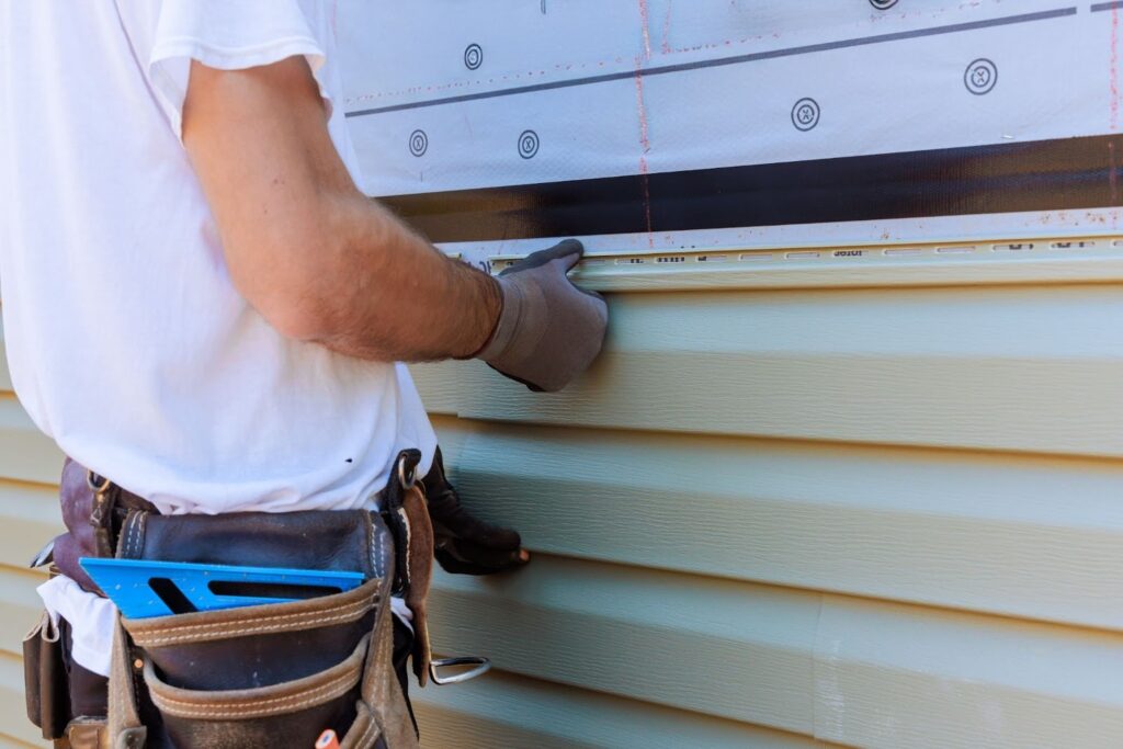 A siding contractor aligning PVC siding panels on a house facade.
