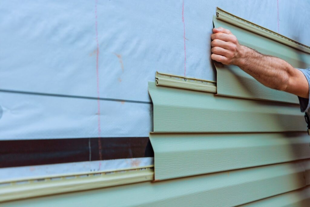 A worker installing vinyl siding on a house.
