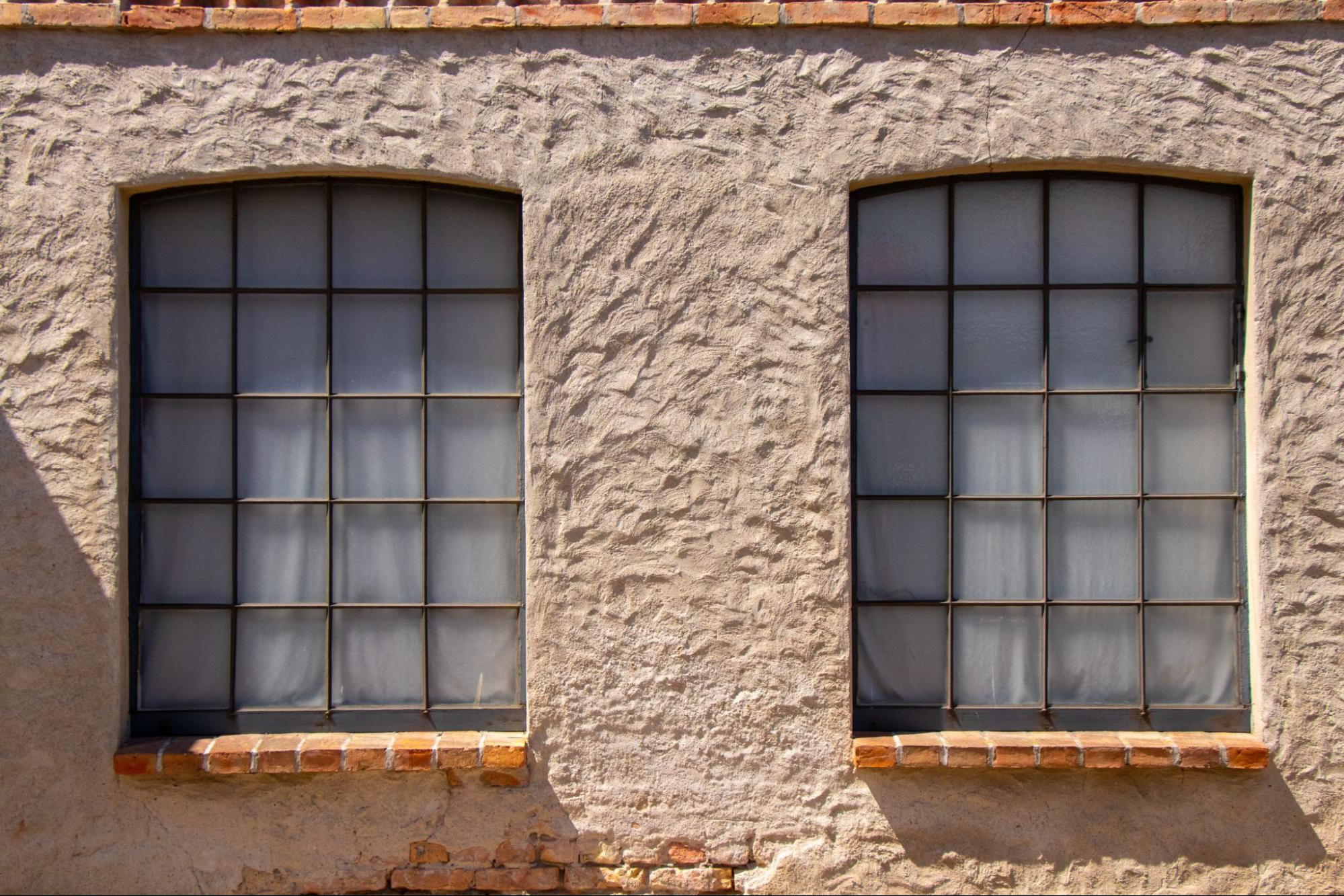 Aged stucco-walled building featuring two barred windows.