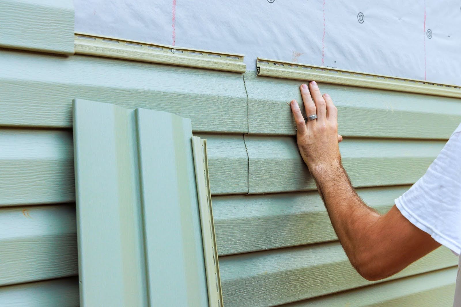 A person's hand is holding a piece of siding against a wall.