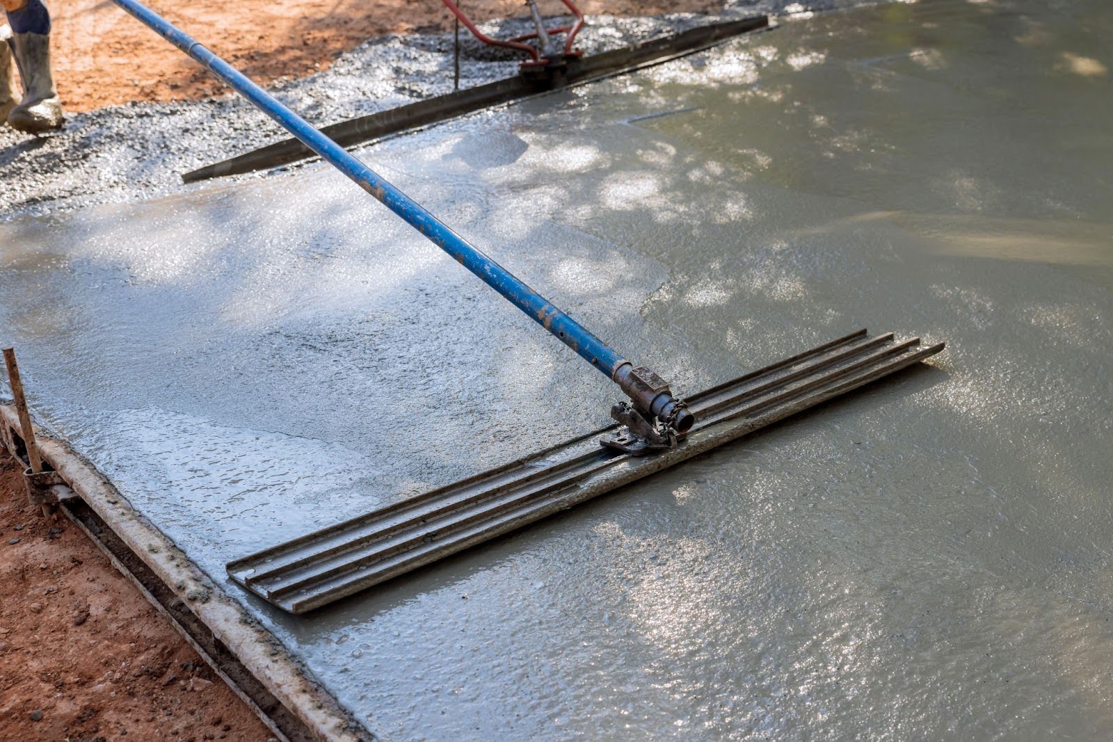 A close-up view of a mason leveling a concrete patio floor with a long trowel.