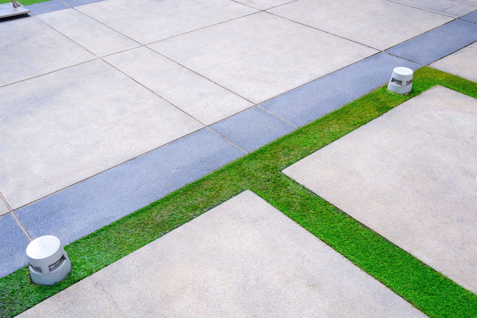 A concrete driveway with grass between sections and lights to enhance design.