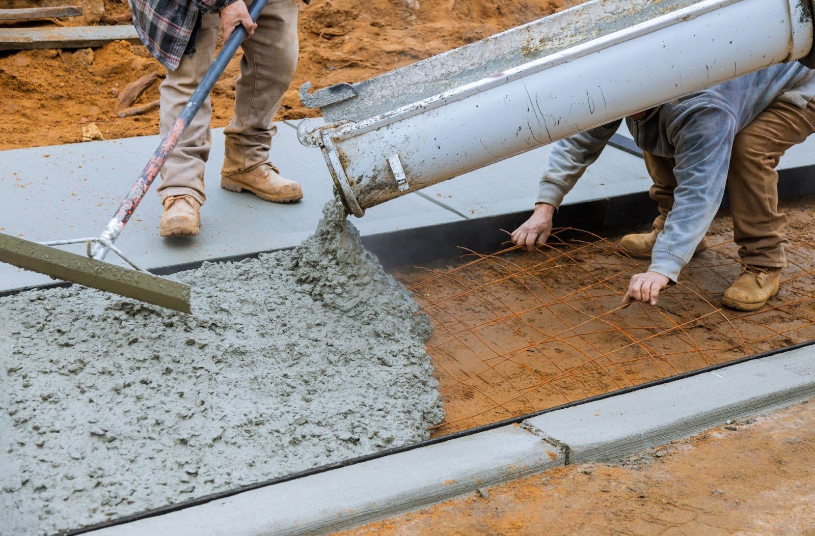 A mixer truck dumps wet cement into a concrete form with workers to prep it.