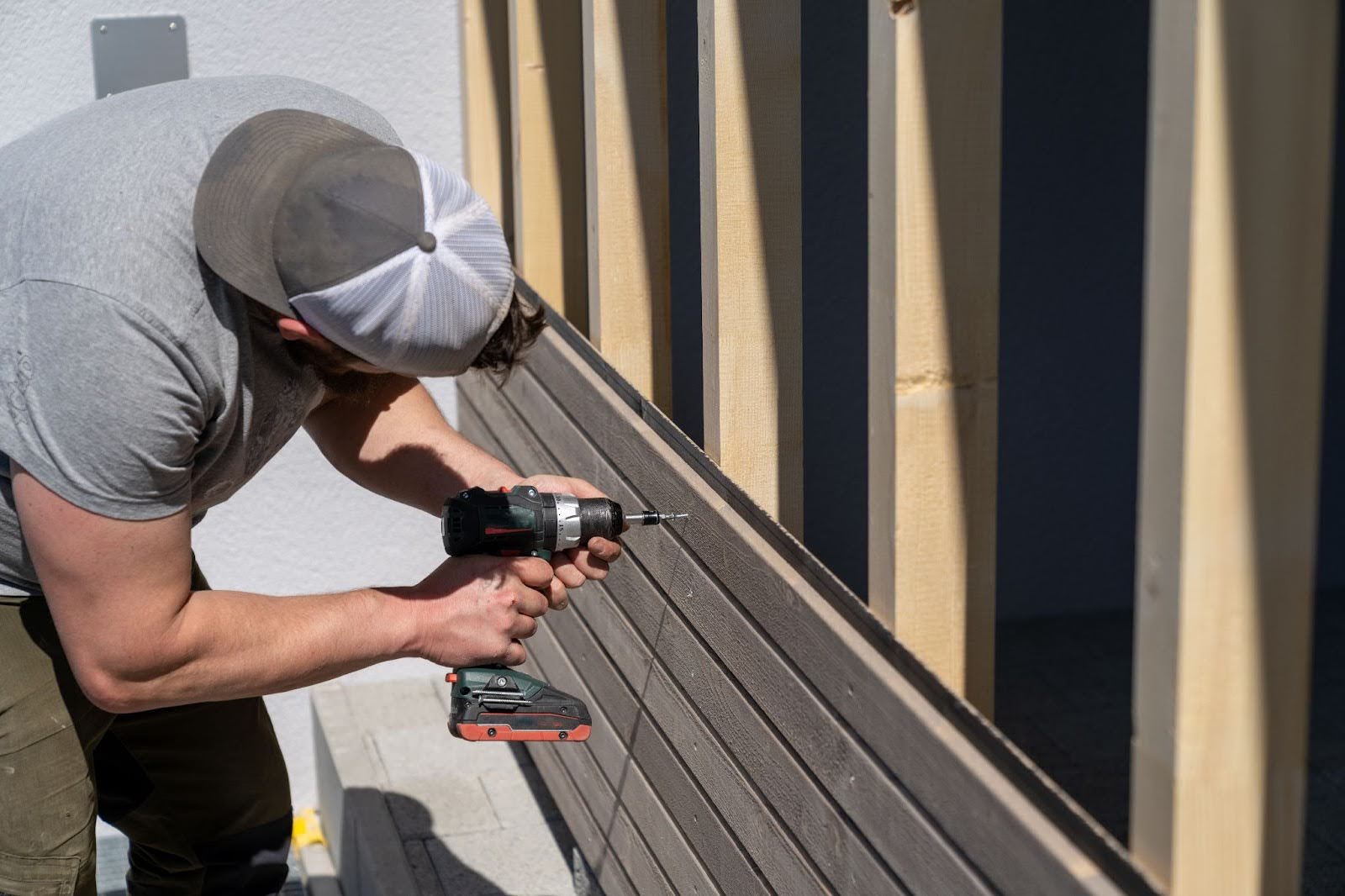 A siding contractor installing wooden siding on a garage using a power drill.