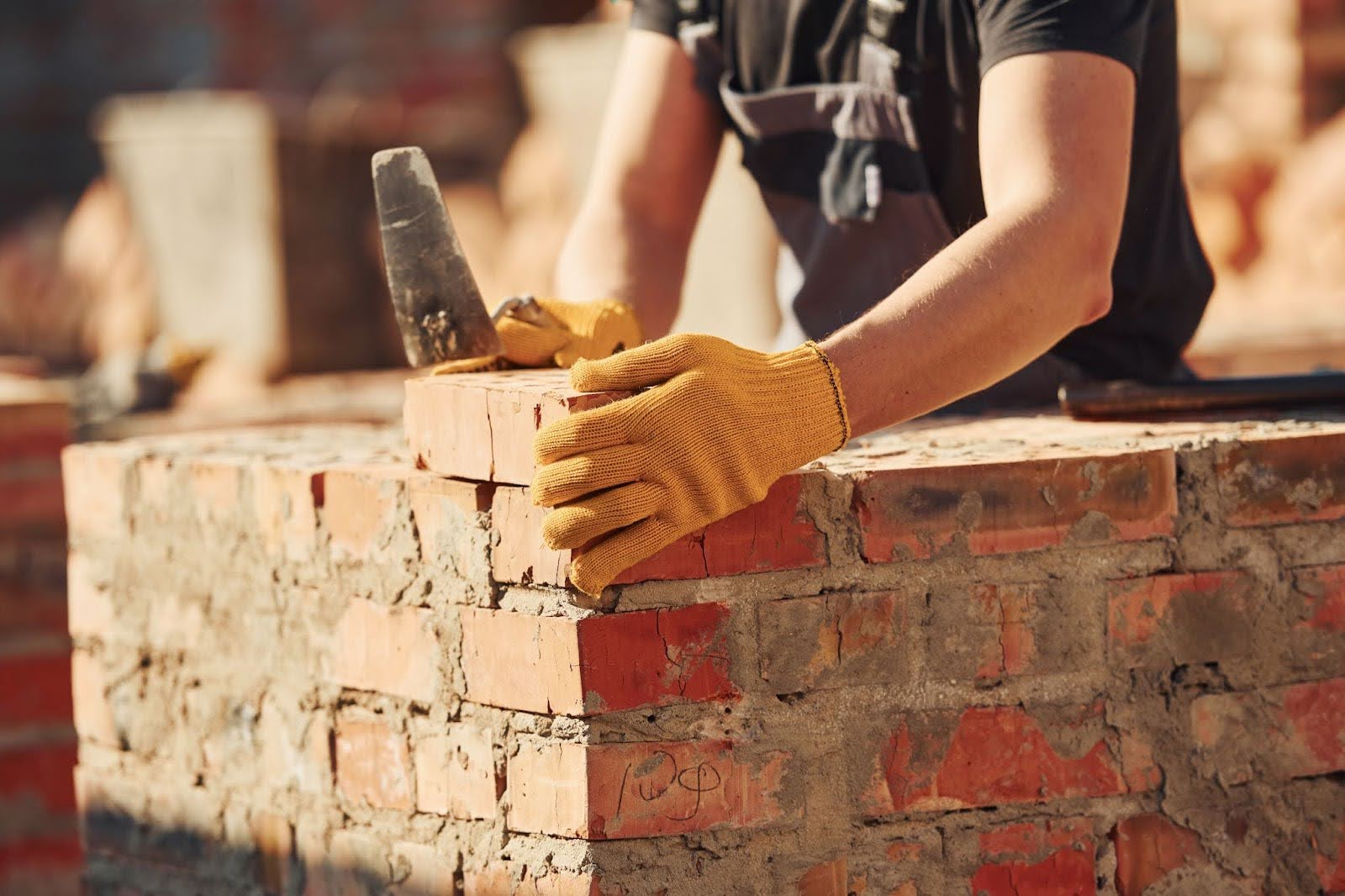A mason in uniform and protective equipment builds a brick wall with precision.